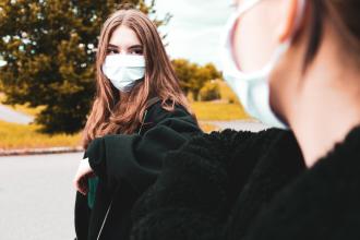
		Schulkinder begrüßen sich mit Maske und Elbogen.
	